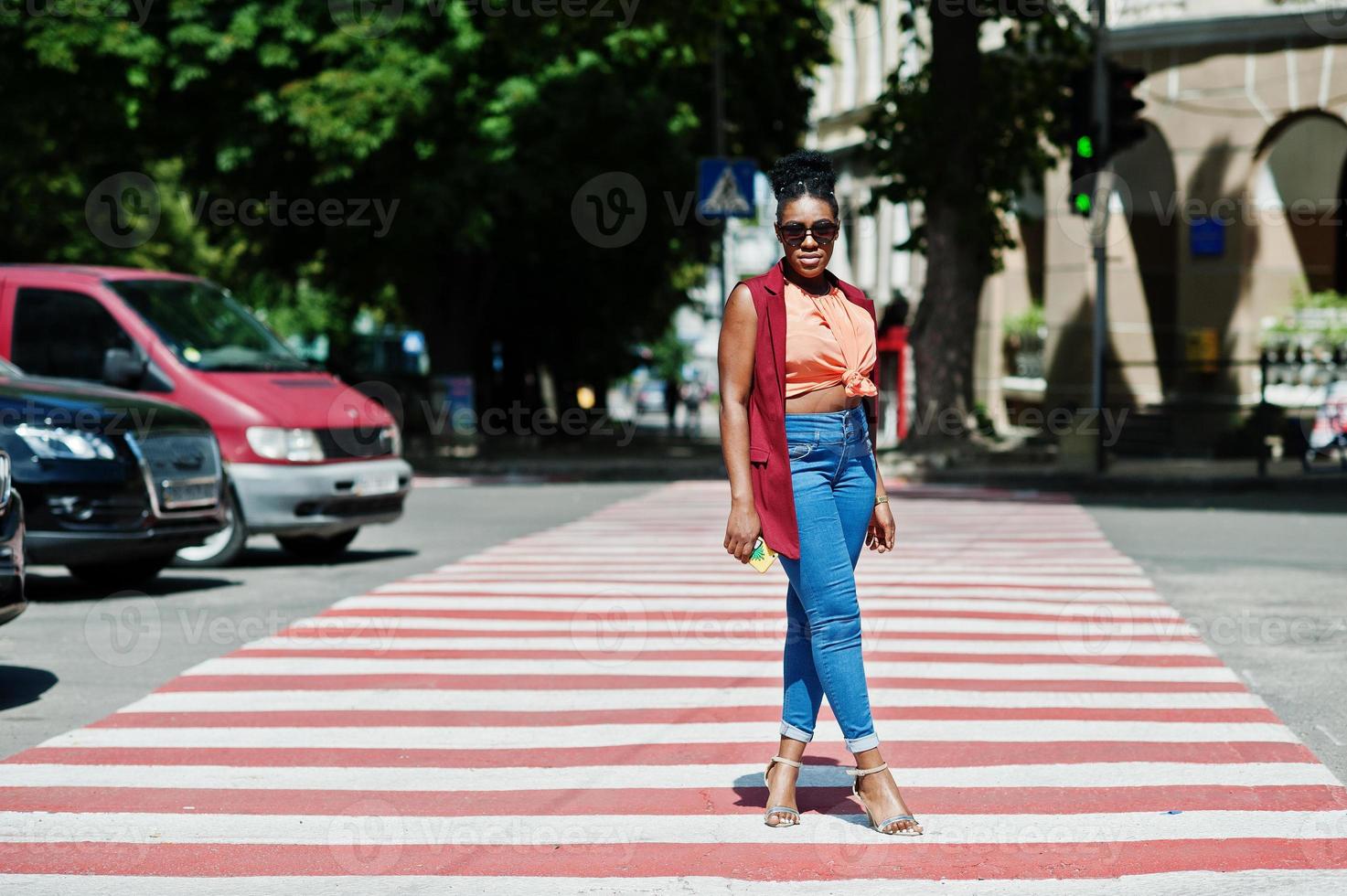 elegante donna afroamericana che cammina sul passaggio pedonale o pedonale con il telefono cellulare a portata di mano. foto