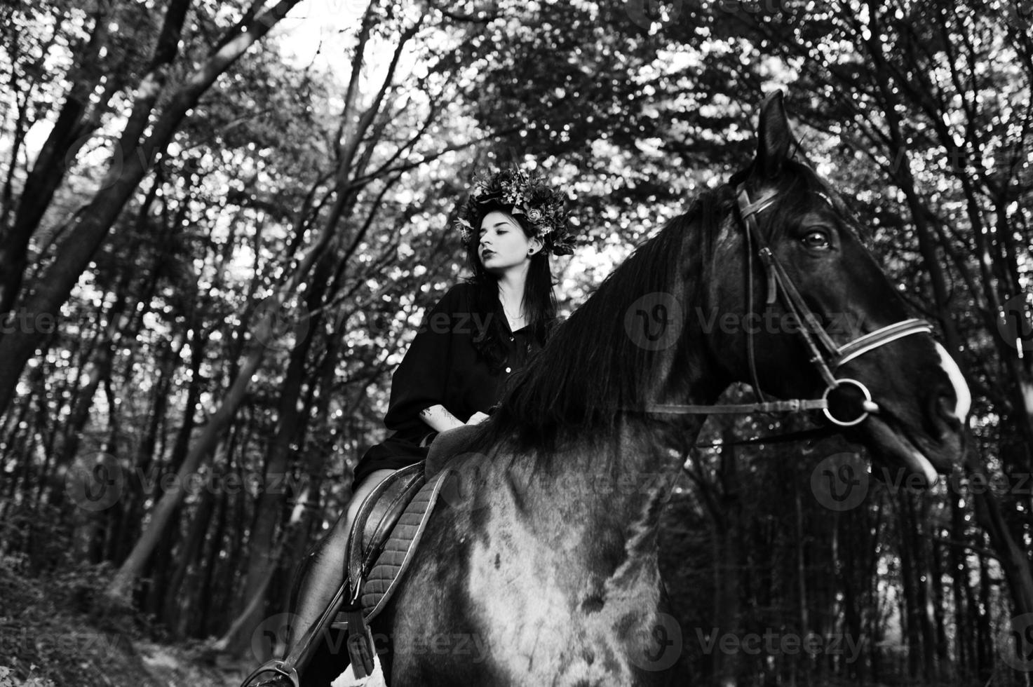 ragazza mistica in ghirlanda indossata in nero a cavallo in legno. foto