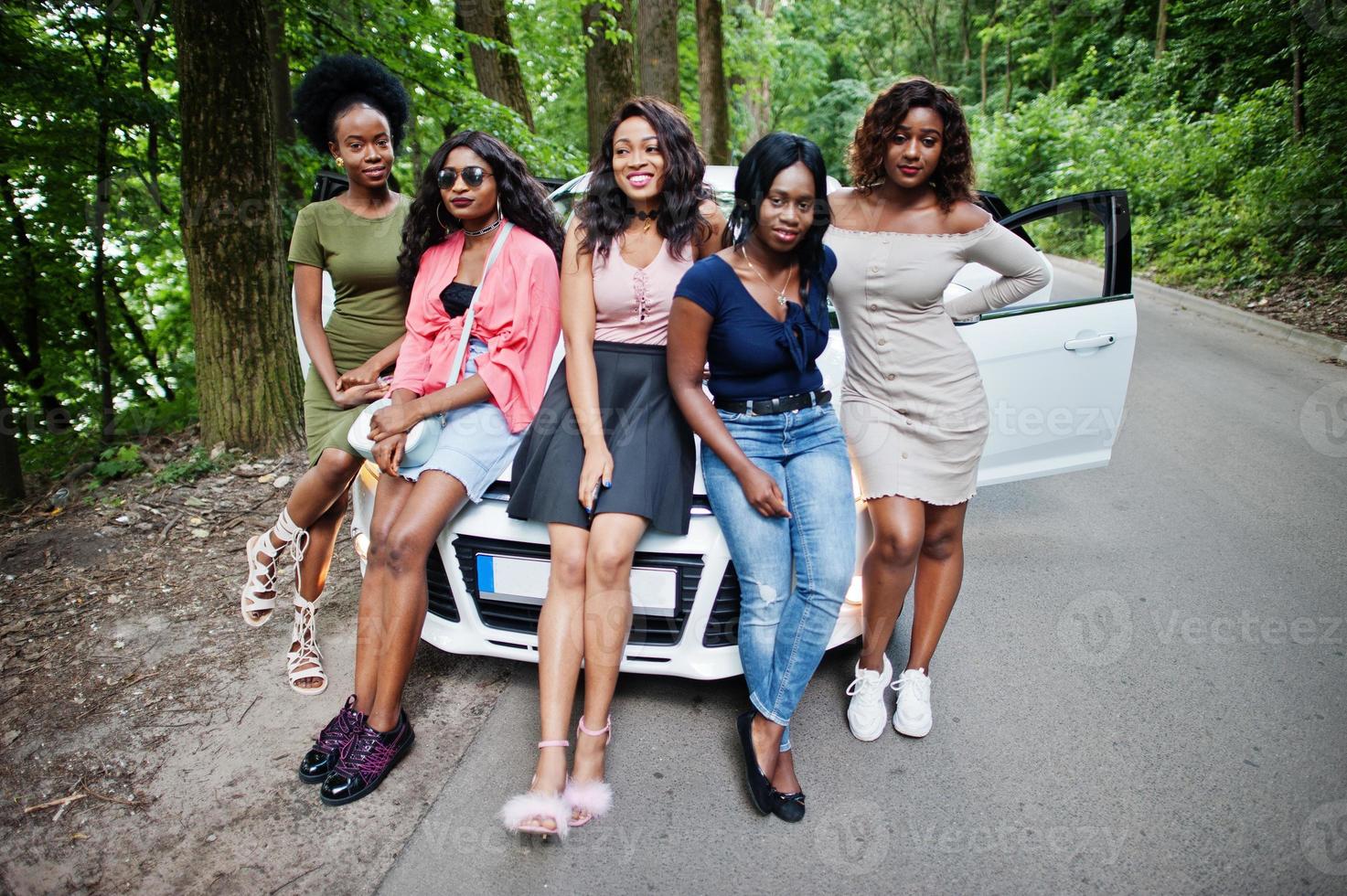 gruppo di cinque ragazze afroamericane felici sedute sul cofano di un'auto. foto