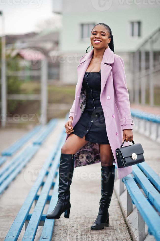 giovane ed elegante bella donna afroamericana in strada alle gradinate dello stadio, indossando un cappotto di moda, tenere la borsa. foto