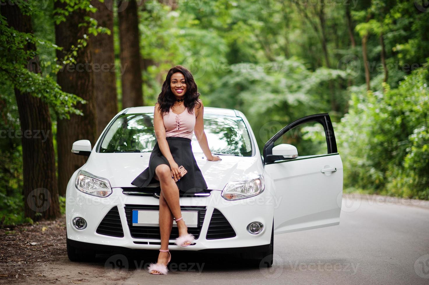 donna afroamericana posata contro un'auto bianca in strada forestale. foto