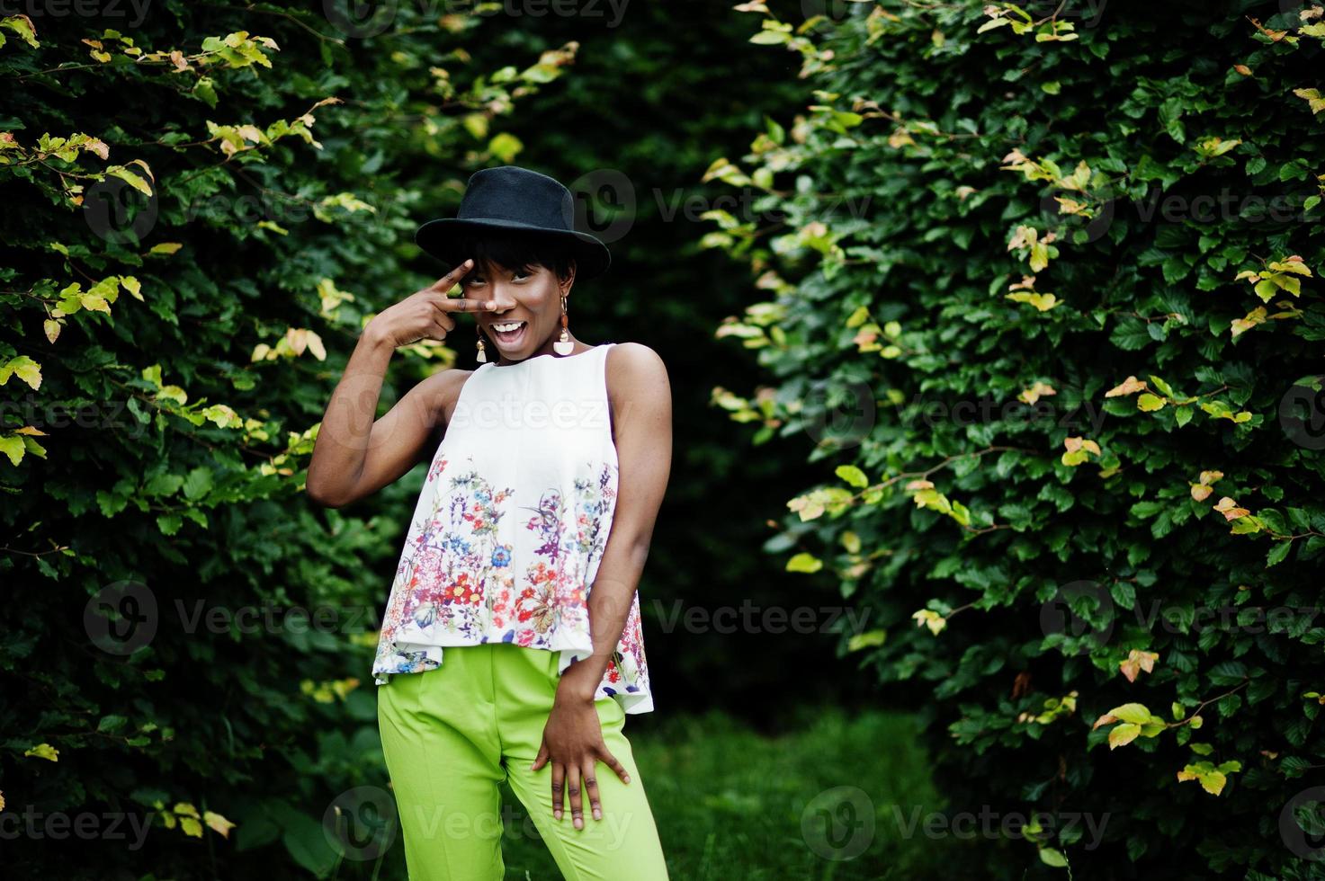 incredibile modella afroamericana in pantaloni verdi e cappello nero in posa con diverse emozioni al parco, mostra due dita. foto