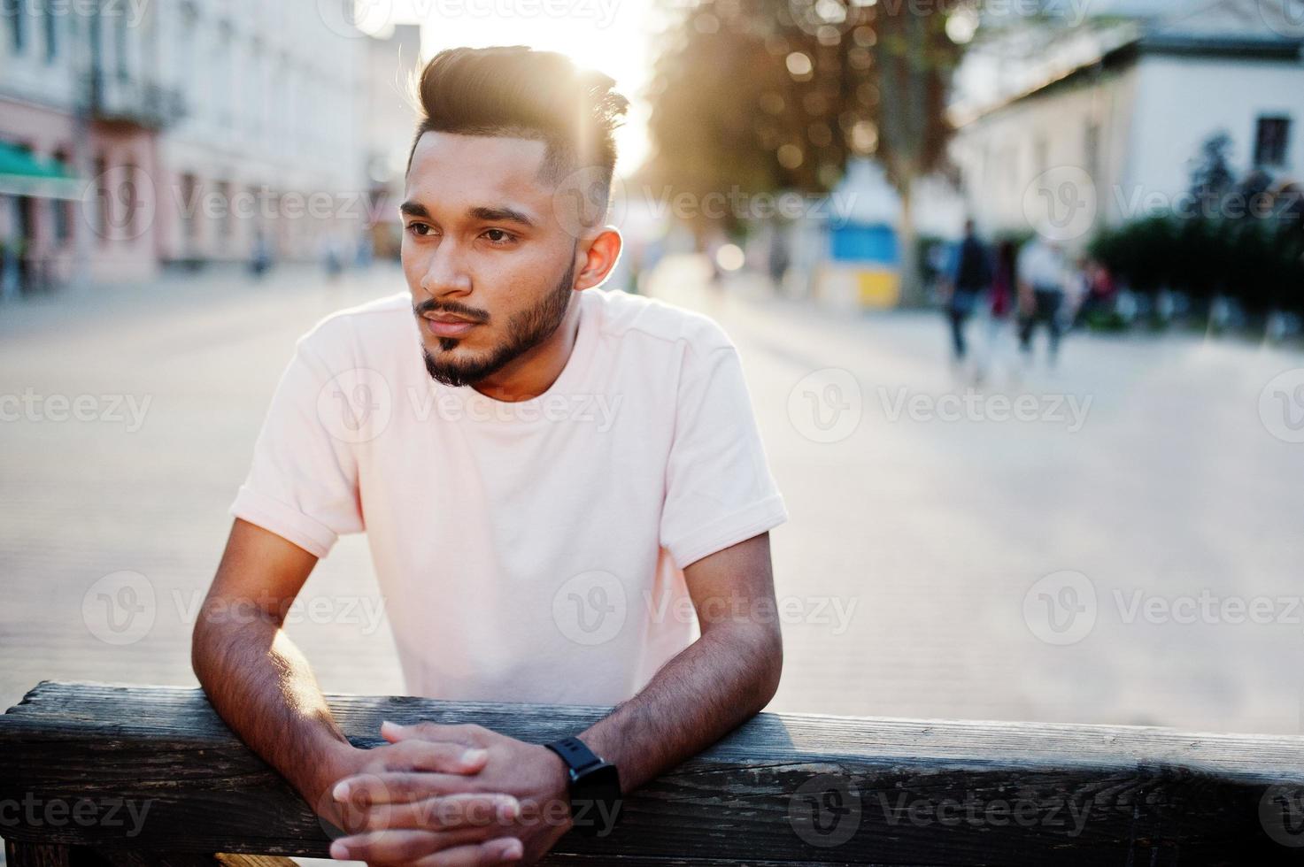 uomo alla moda con barba indiana in maglietta rosa. modello indiano posato all'aperto nelle strade del tramonto della città. foto