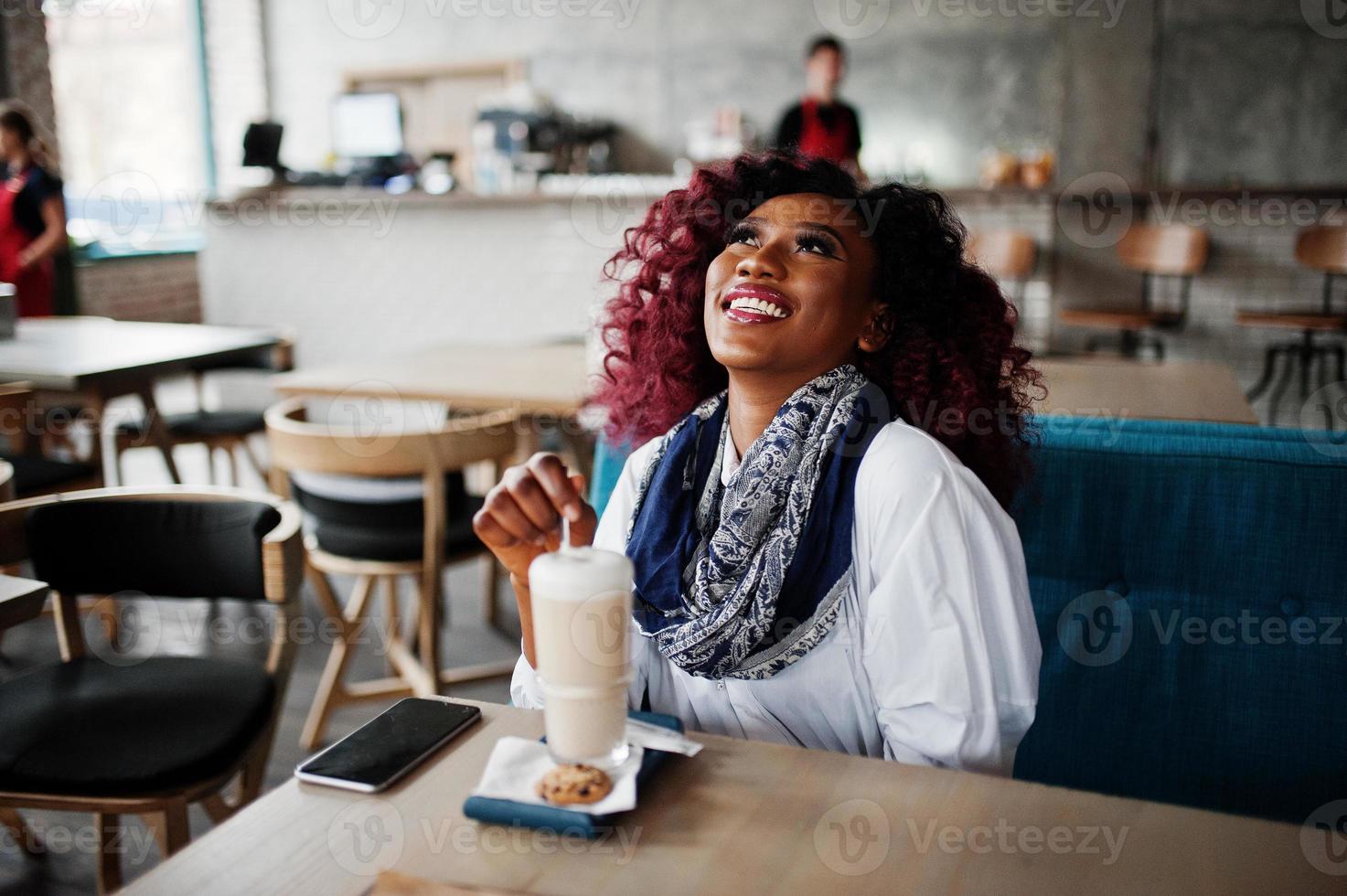 attraente ragazza riccia afroamericana seduta al caffè con latte. foto