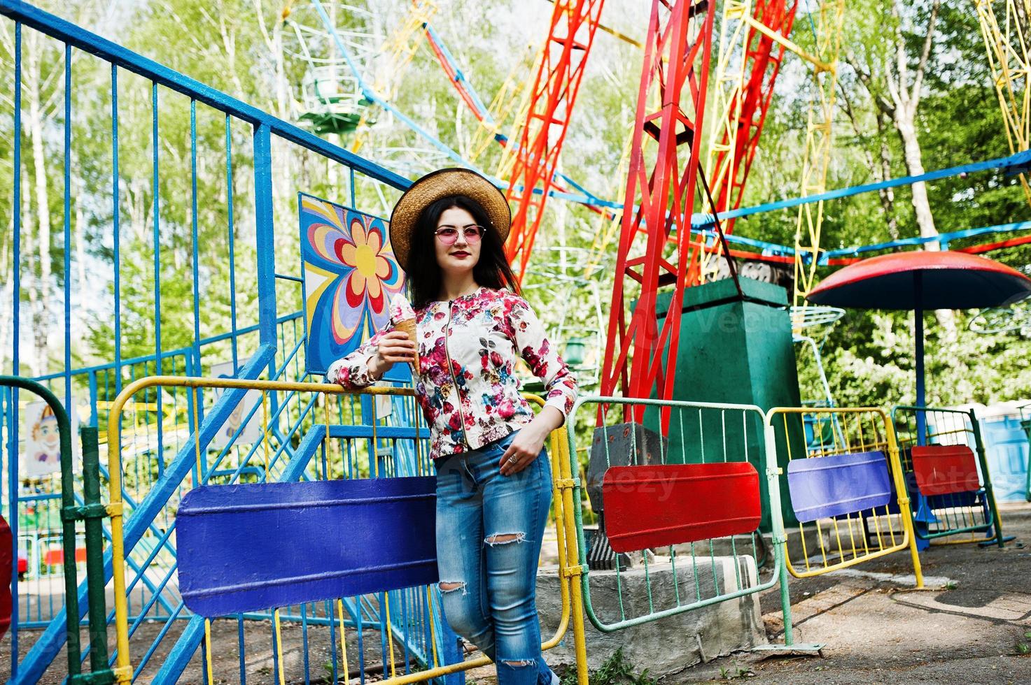 ritratto di ragazza bruna con occhiali rosa e cappello con gelato al parco divertimenti. foto