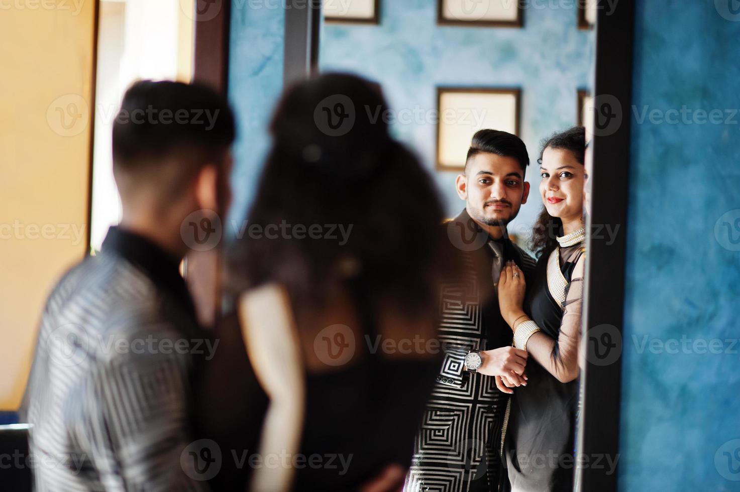 adorabile coppia indiana innamorata, indossata a saree e abito elegante, posata al ristorante e guardando allo specchio. foto