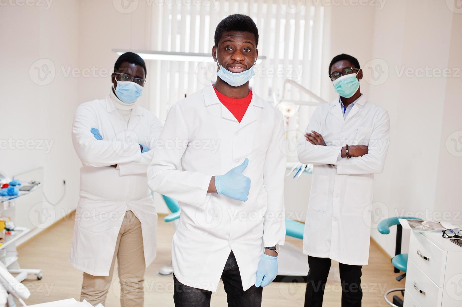 tre medici maschi afroamericani con le braccia incrociate in clinica odontoiatrica. mostra il pollice in su. foto
