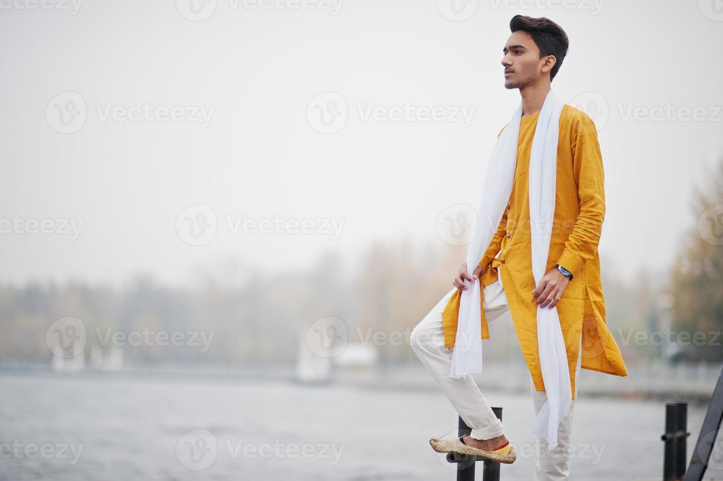 uomo indiano alla moda in abiti tradizionali gialli con sciarpa bianca poste all'aperto contro il molo nebbioso del mare. foto