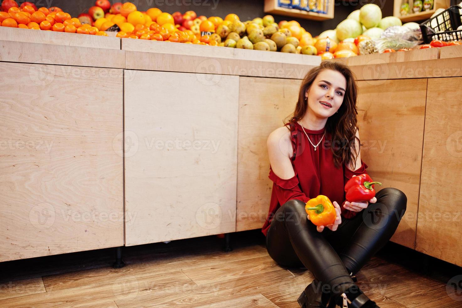 ragazza in rosso che tiene due peperoni sul negozio di frutta. foto