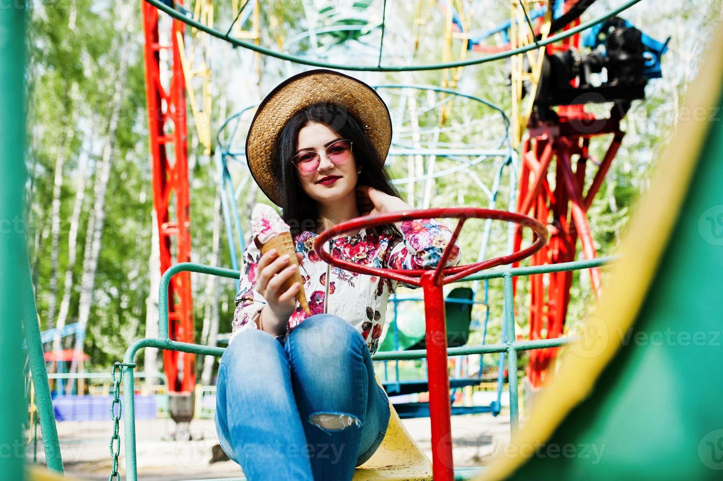 ritratto di ragazza bruna con occhiali rosa e cappello con gelato al parco divertimenti. foto