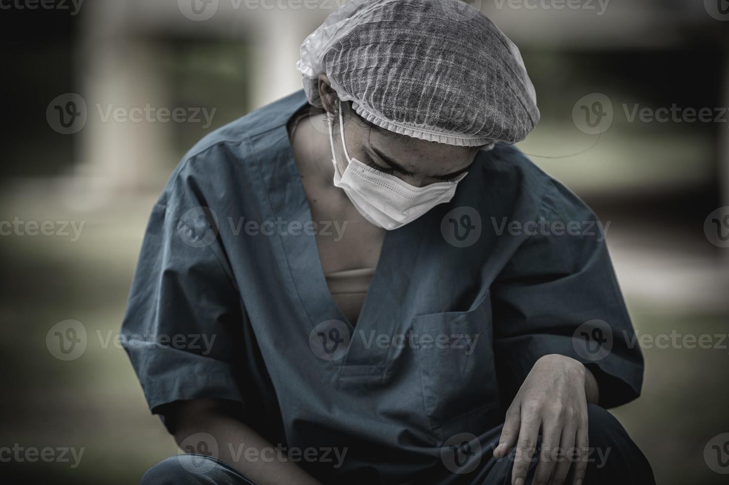 stanco depresso donna asiatica scrub infermiera indossa maschera facciale uniforme blu siede sul pavimento dell'ospedale, giovane donna medico stressato dal duro lavoro foto