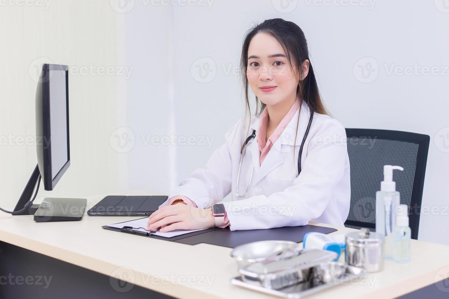 medico femminile sorridente giovane e bello asiatico che si siede nell'ufficio all'ospedale. foto