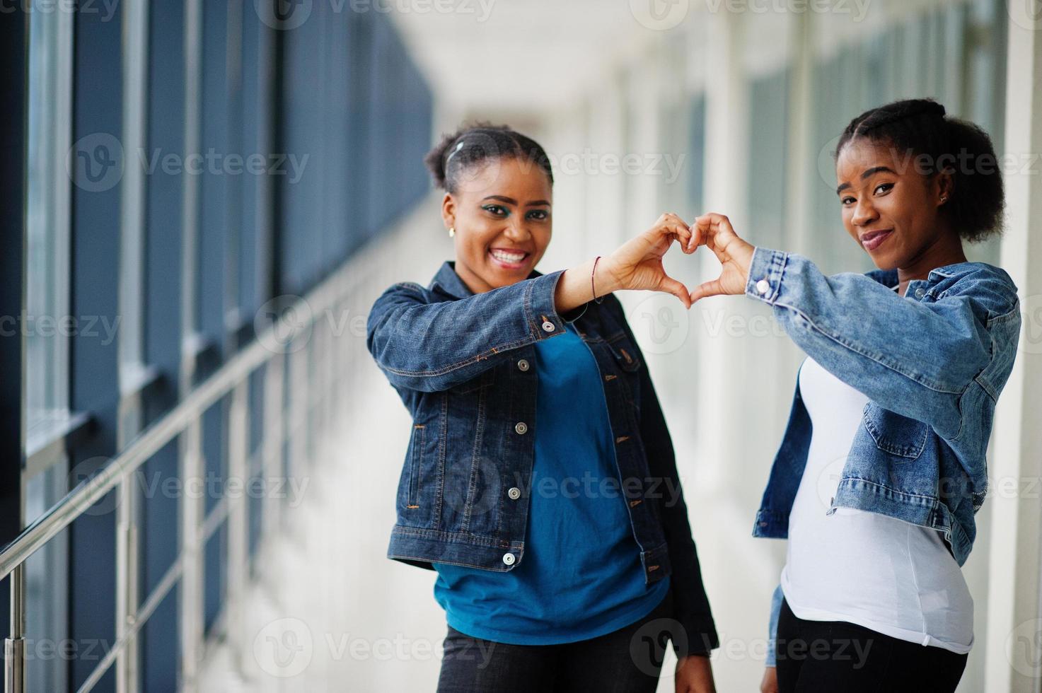 due amiche africane in giacca di jeans che mostrano il cuore con le dita al coperto insieme. foto