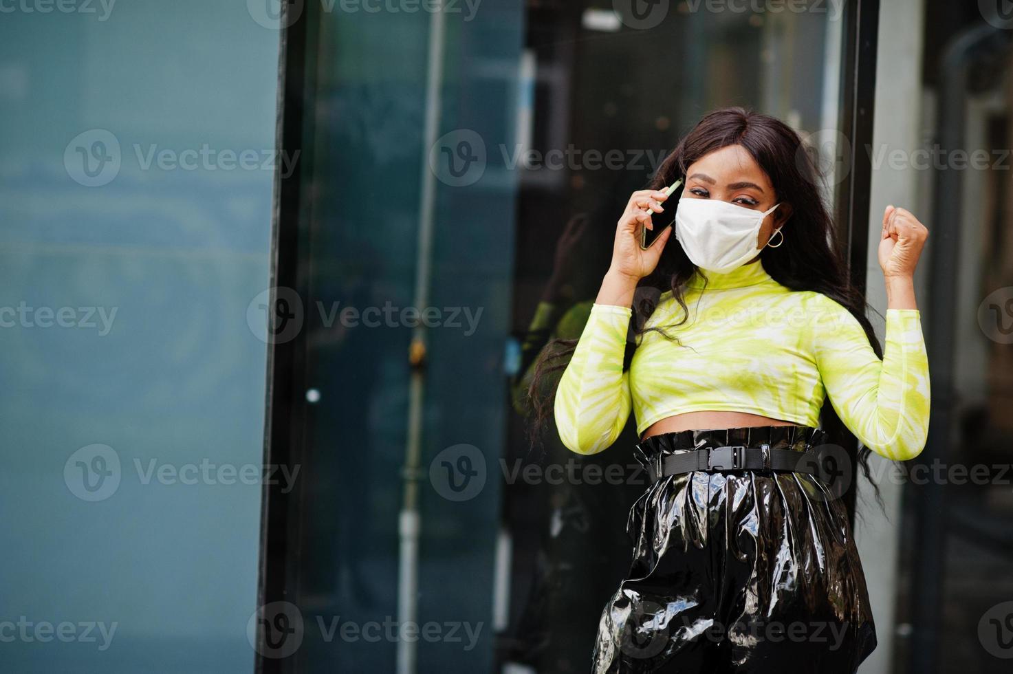 donna afroamericana in posa con maschera facciale per proteggere da infezioni da batteri, virus ed epidemie e tenere il telefono cellulare. foto