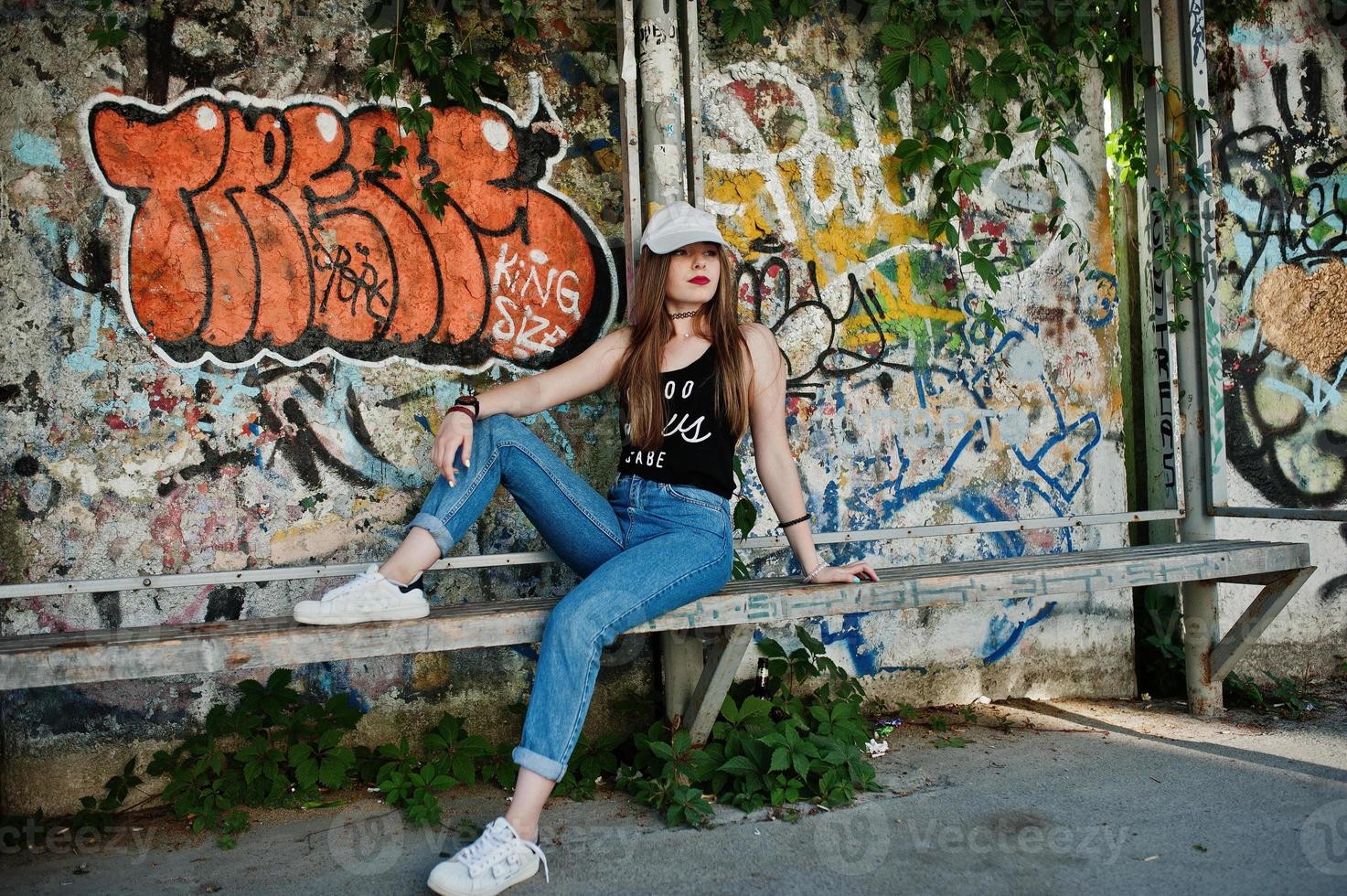 ragazza hipster casual alla moda in berretto e jeans indossano contro un grande muro di graffiti. foto