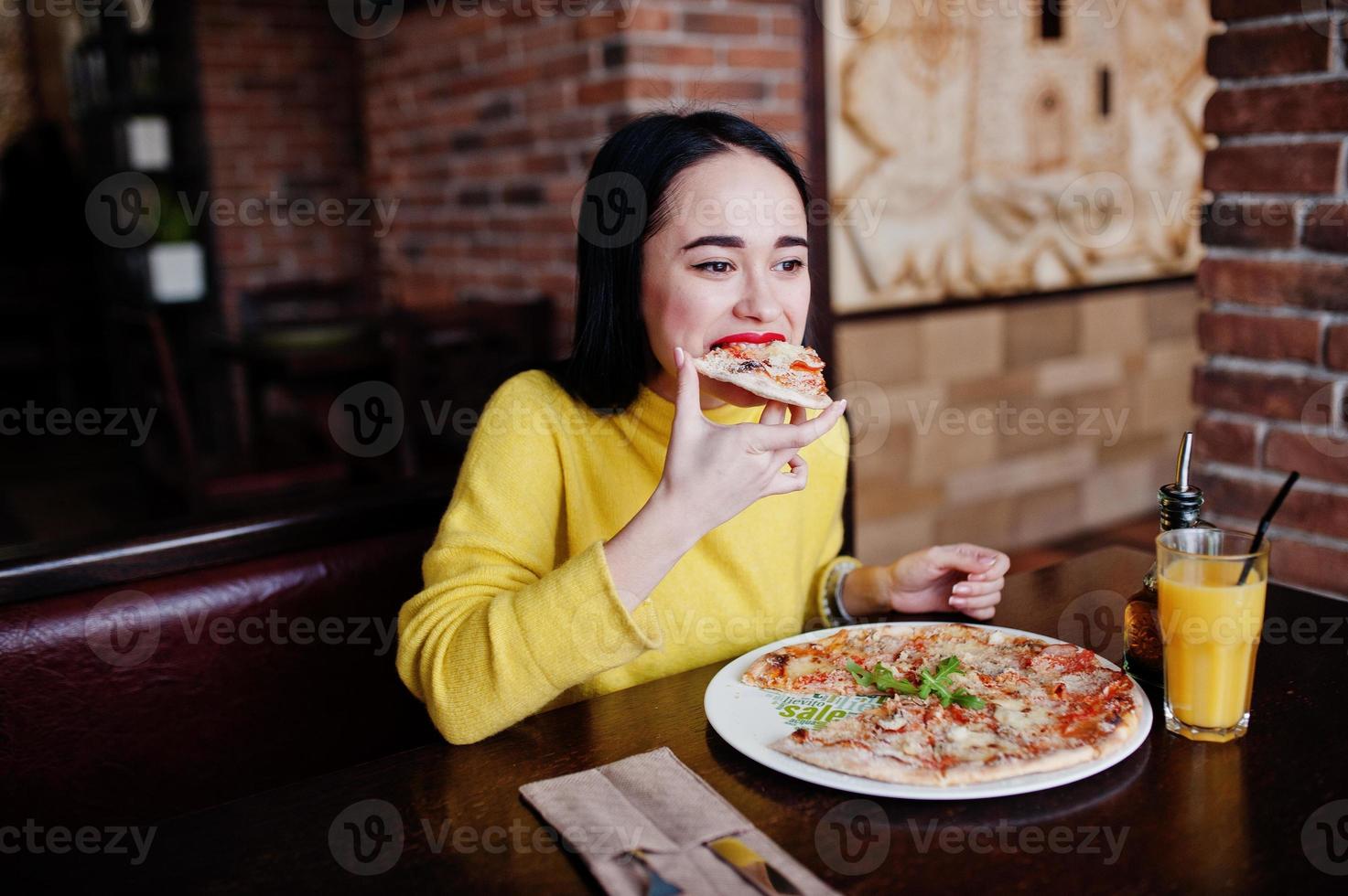 divertente ragazza bruna in maglione giallo che mangia pizza al ristorante. foto