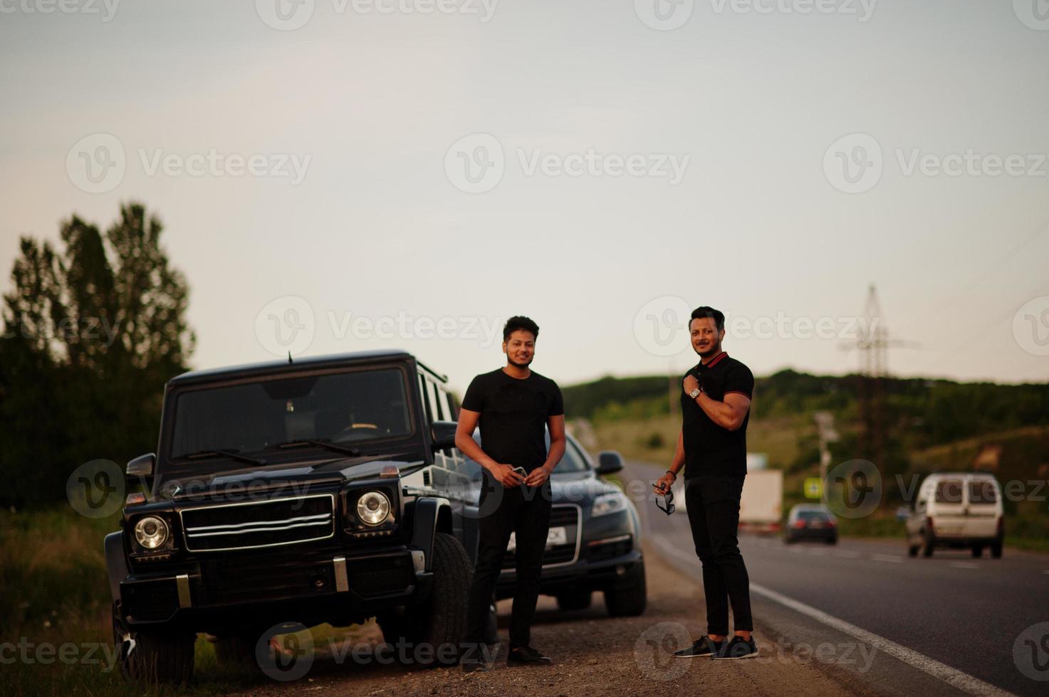 due fratelli asiatici indossano un uomo tutto nero in posa vicino alle auto suv. foto