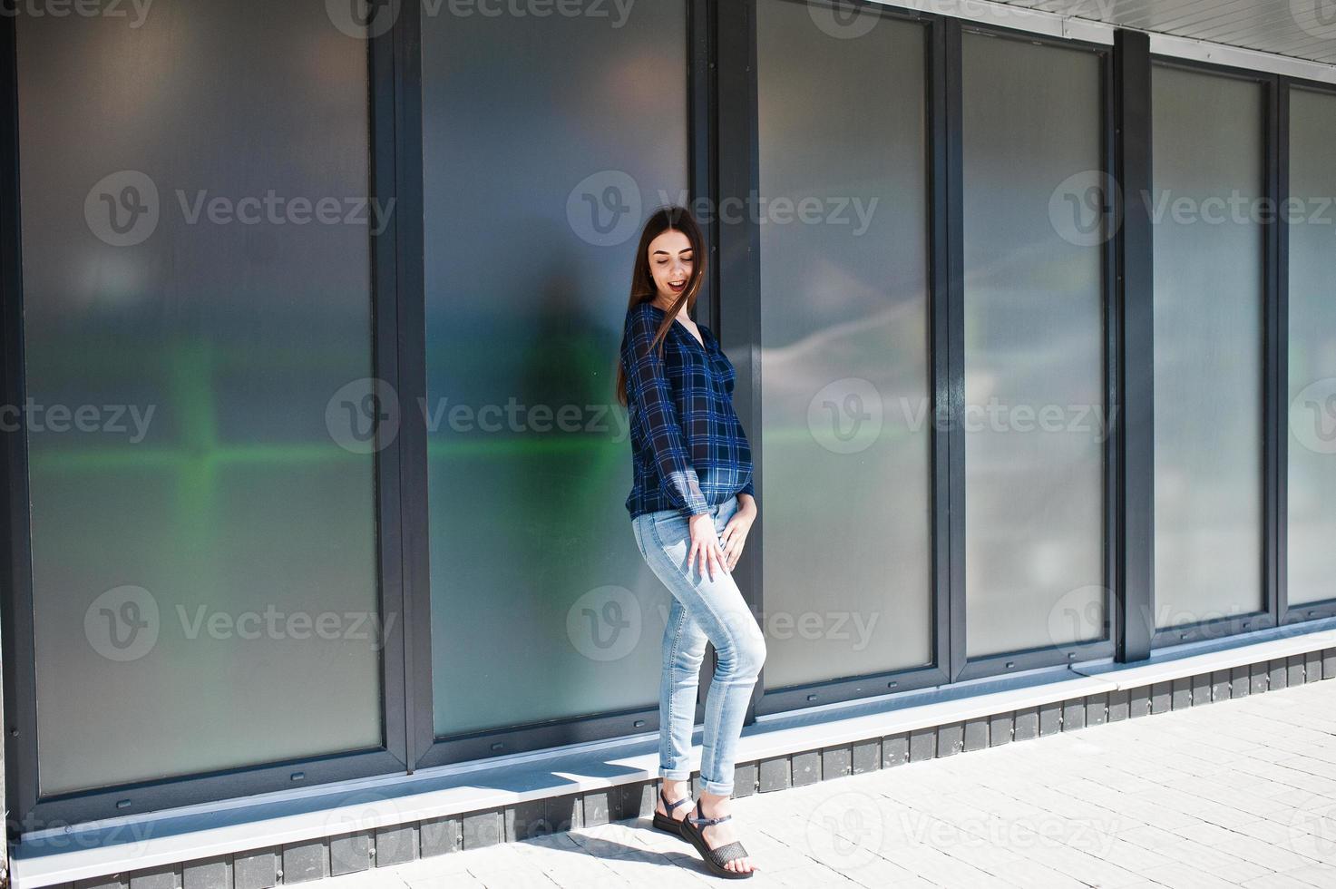 ritratto di giovane ragazza bruna in camicia a scacchi blu contro grandi finestre. foto