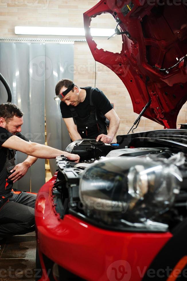 l'addetto al servizio di auto ha messo una pellicola anti ghiaia su una carrozzeria rossa presso l'officina del veicolo di dettaglio. protezione dell'auto con pellicole speciali. foto