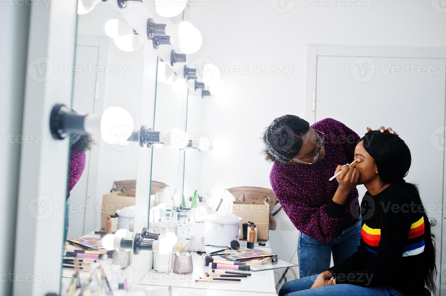 donna afroamericana che applica il trucco dal truccatore al salone di bellezza. foto
