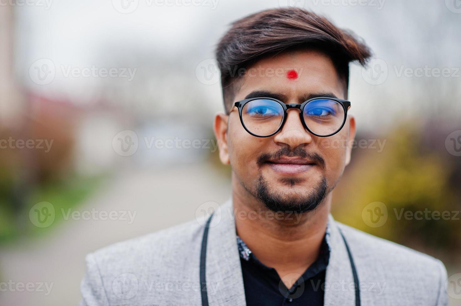 primo piano testa di elegante uomo indiano con bindi sulla fronte e occhiali, indossare su tuta posata all'aperto. foto