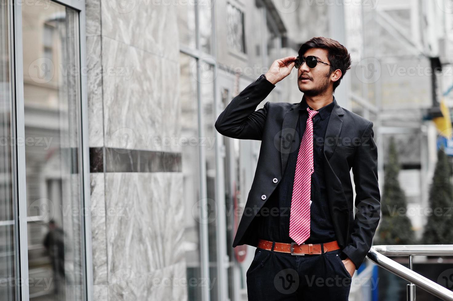 giovane indiano in abito, cravatta e occhiali da sole in posa all'aperto. foto