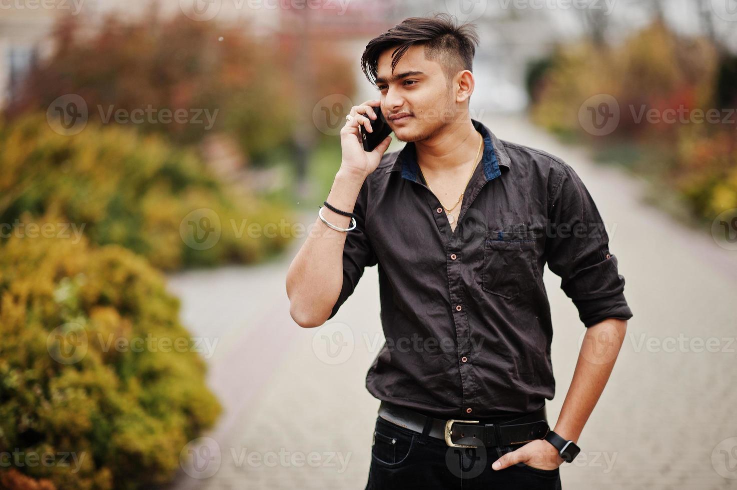 uomo indiano in camicia marrone posato all'aperto e parlando sul telefono cellulare. foto