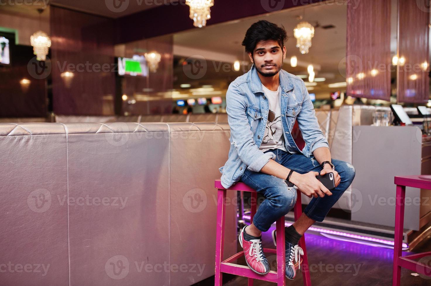 elegante uomo asiatico indossare sulla giacca di jeans seduto su una sedia contro il bar nel club. foto