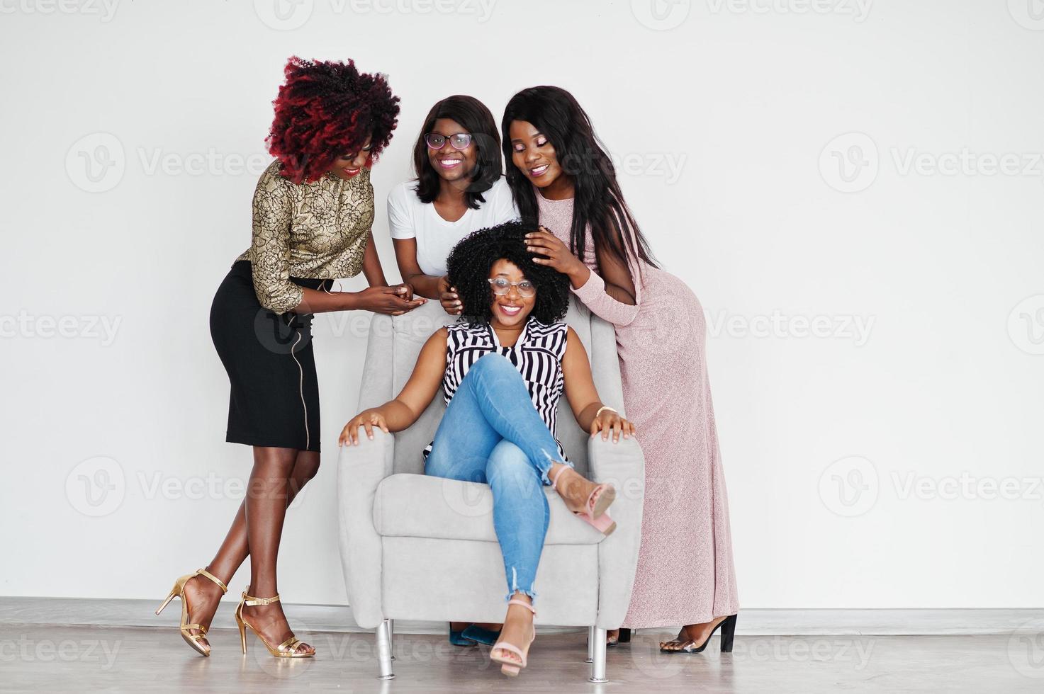 felici momenti positivi luminosi di quattro ragazze africane. divertirsi e sorridere sulla sedia contro il muro bianco vuoto. bei momenti di quattro migliori amici. foto