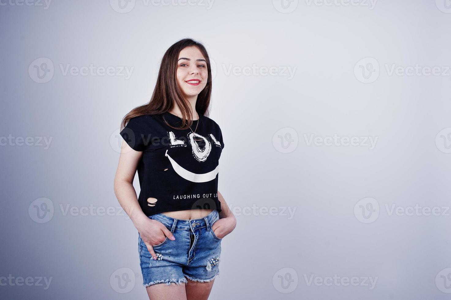 ritratto di una ragazza attraente in maglietta nera che dice lol e pantaloncini di jeans in posa in studio. foto
