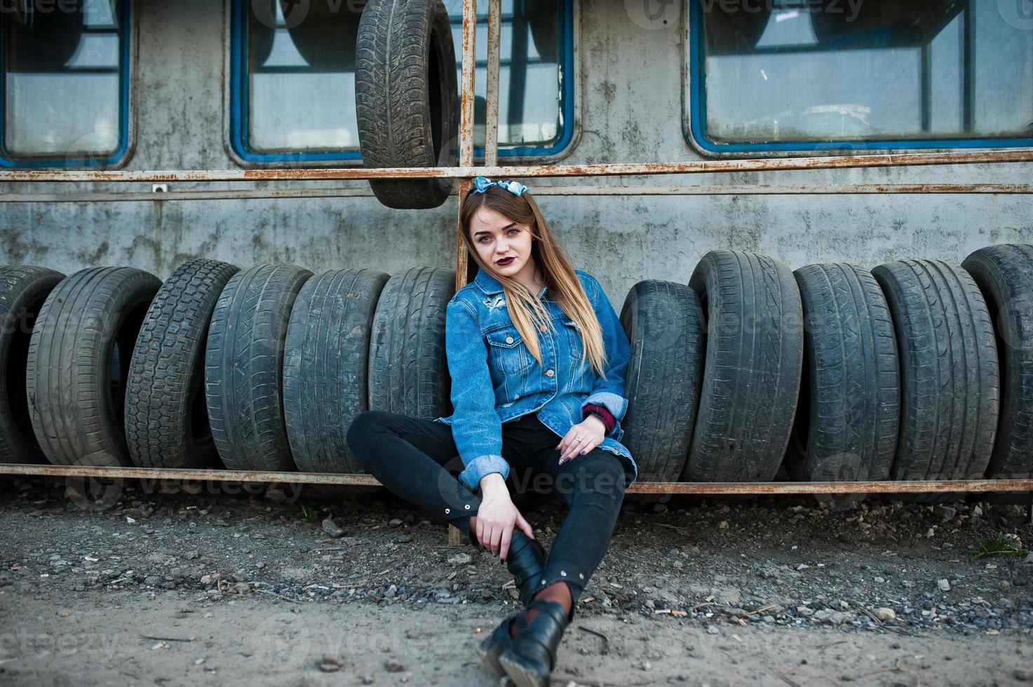 giovane ragazza hipster in giacca di jeans e sciarpa per la testa nella zona di montaggio dei pneumatici. foto