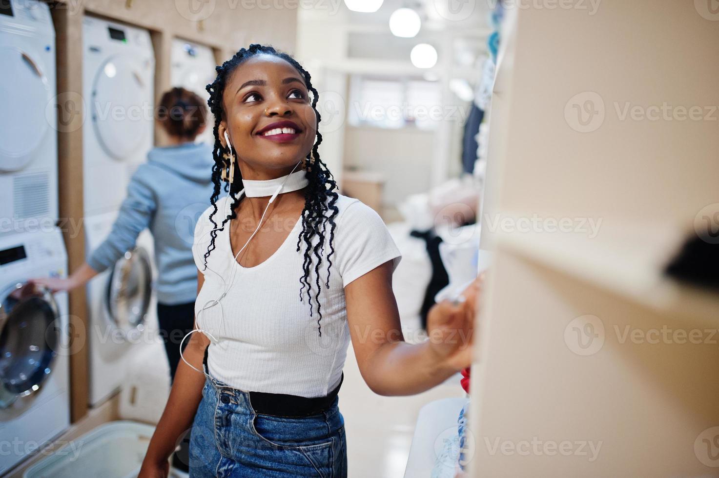 allegra donna afroamericana tenere detersivo vicino alla lavatrice nella lavanderia self-service. foto