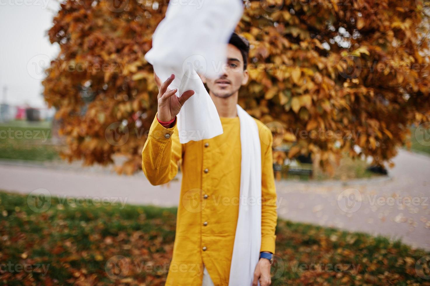 uomo indiano alla moda in abiti tradizionali gialli con sciarpa bianca posata all'aperto contro le foglie autunnali. foto