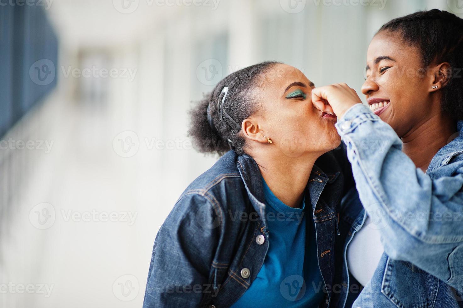 due amiche africane in giacca di jeans prendono il naso insieme al coperto. foto