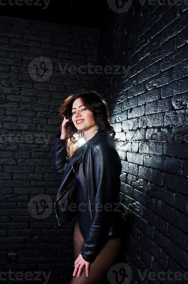 ritratto in studio di ragazza bruna sexy in giacca di pelle nera contro il muro di mattoni. foto