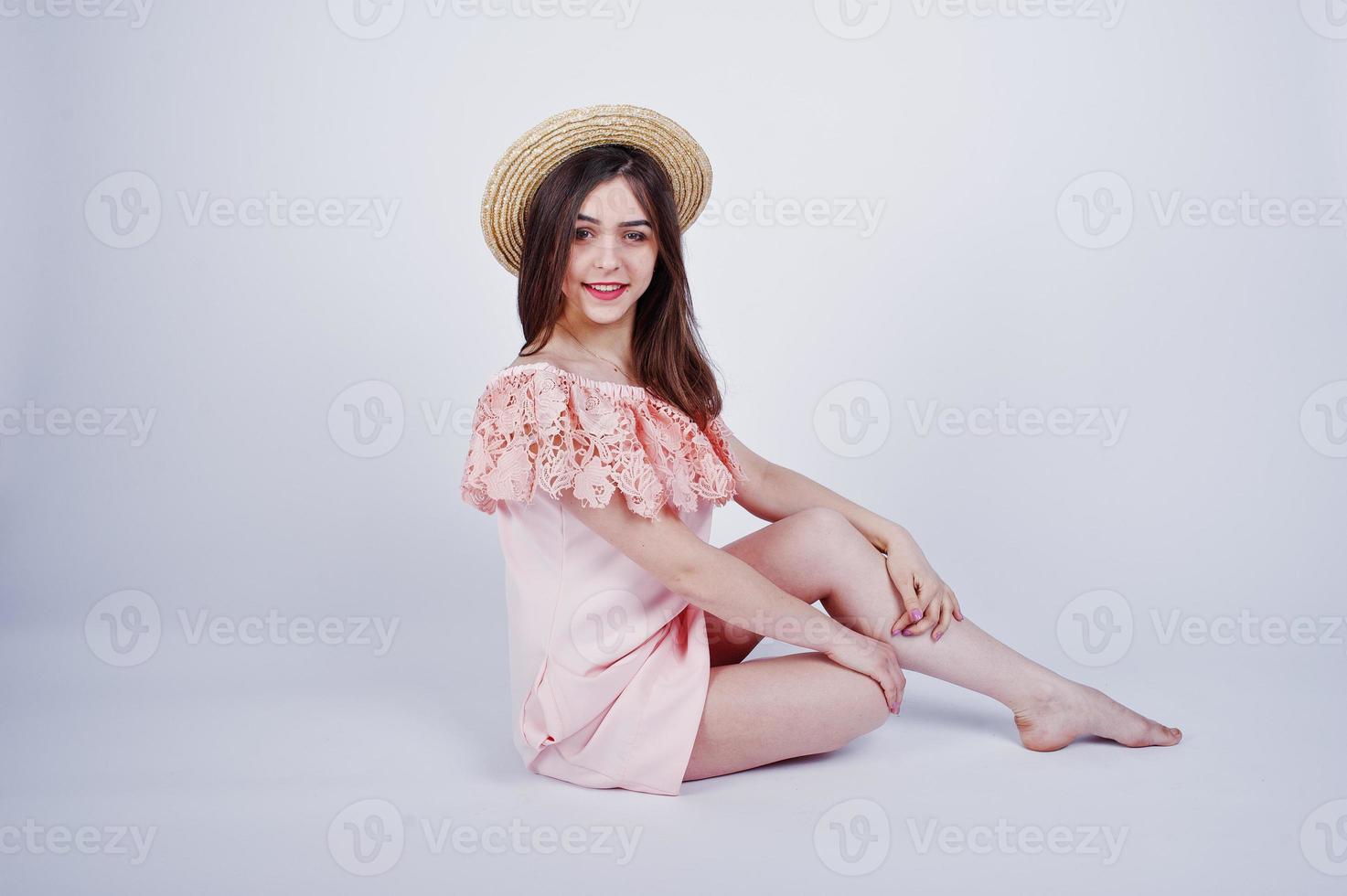 ritratto di una donna alla moda in abito rosa seduta e in posa con un cappello sul pavimento in studio. foto