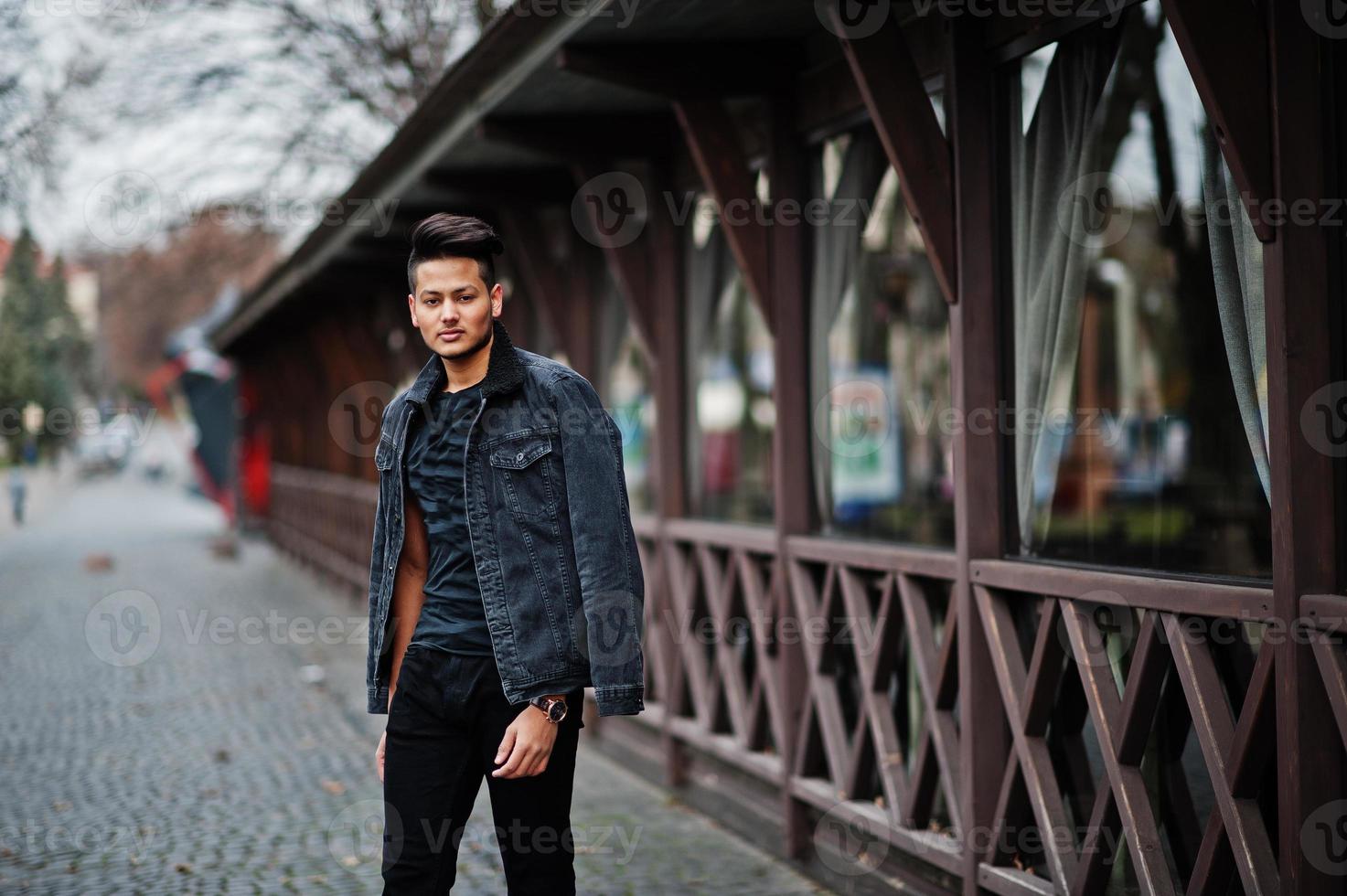 uomo indiano bello e alla moda in giacca di jeans nera posata all'aperto. foto