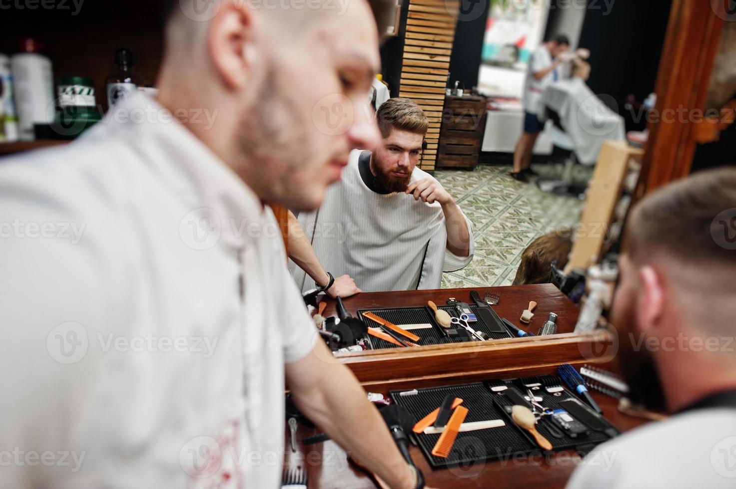 giovane uomo barbuto che si fa tagliare i capelli dal parrucchiere mentre è seduto su una sedia al barbiere. anima da barbiere. foto