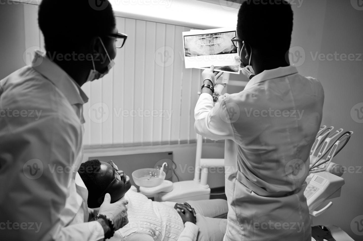 paziente uomo afroamericano in poltrona odontoiatrica. studio dentistico e concetto di pratica medica. dentista professionista che aiuta il suo paziente in odontoiatria medica. indicando la radiografia dei denti. foto