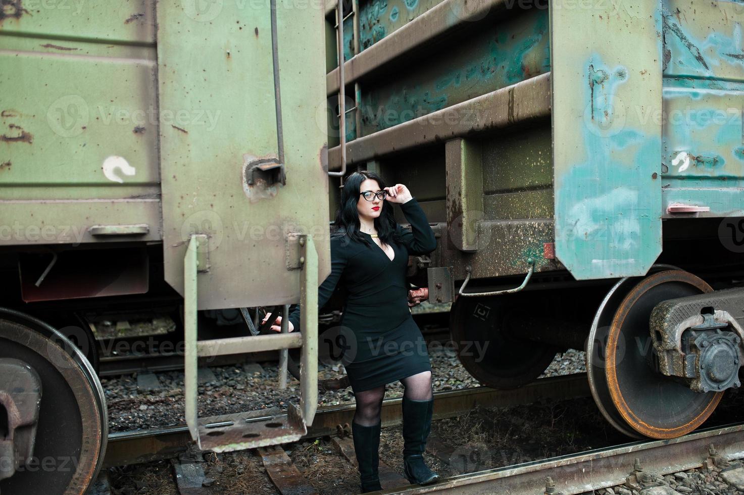 ragazza bruna indossa in nero con gli occhiali nella stazione ferroviaria. foto