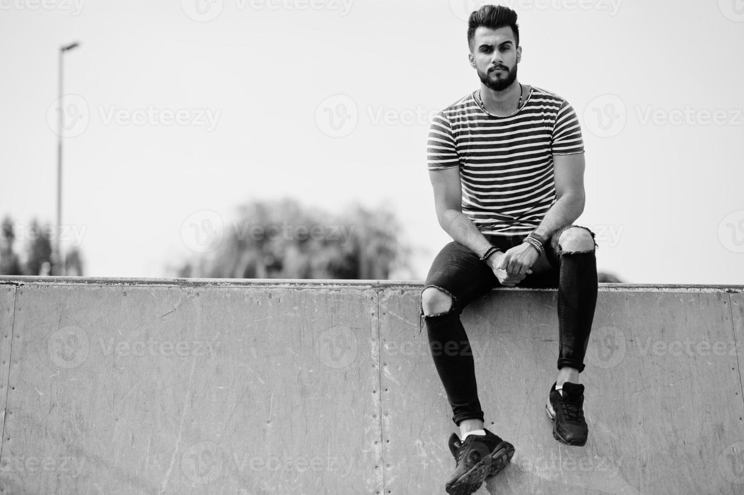 modello di uomo bello e alto con barba araba in camicia spogliata in posa all'aperto allo skate park. ragazzo arabo alla moda. foto