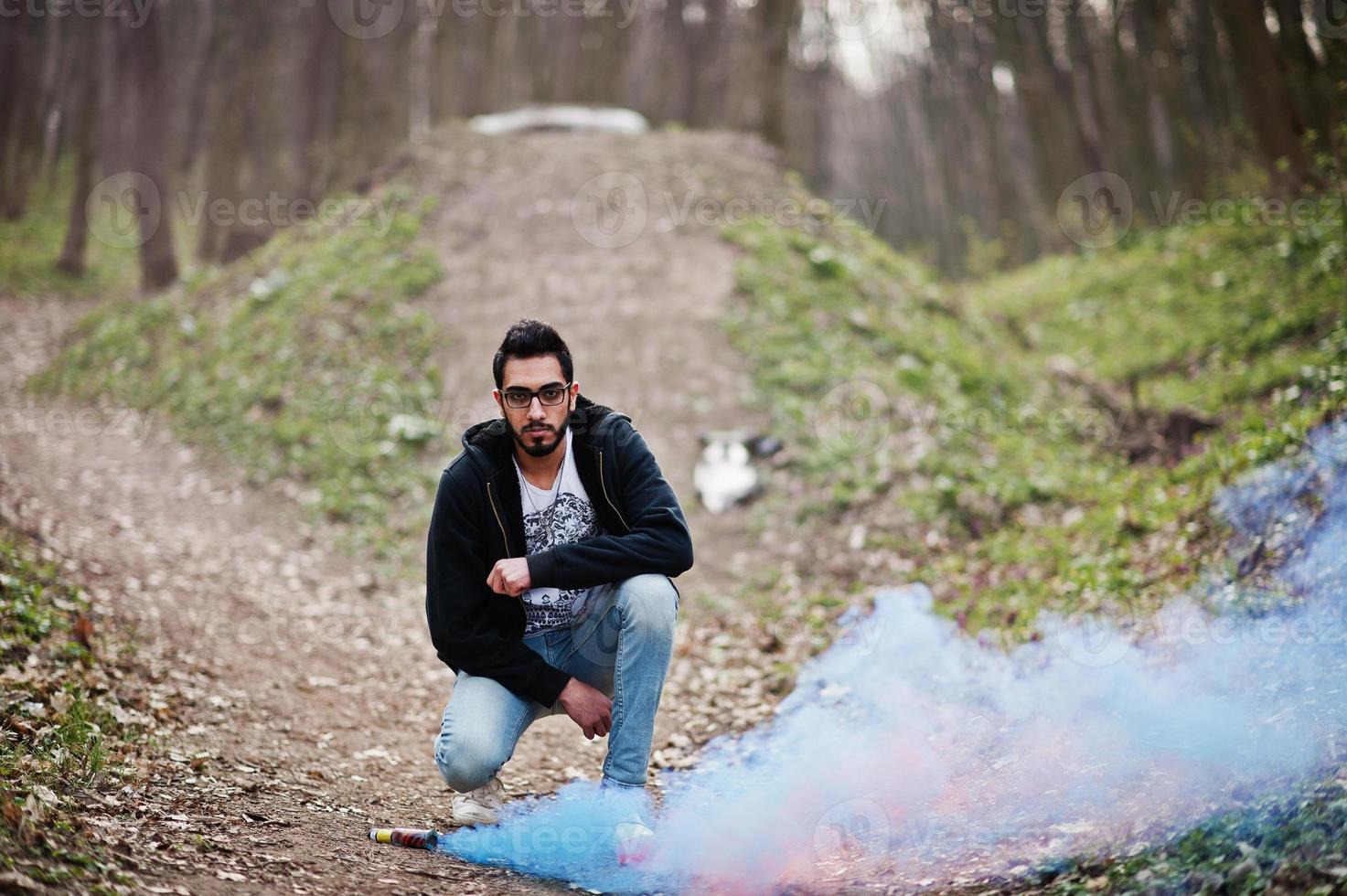 l'uomo arabo di street style con gli occhiali tiene il bagliore della mano con una bomba fumogena rossa e blu. foto