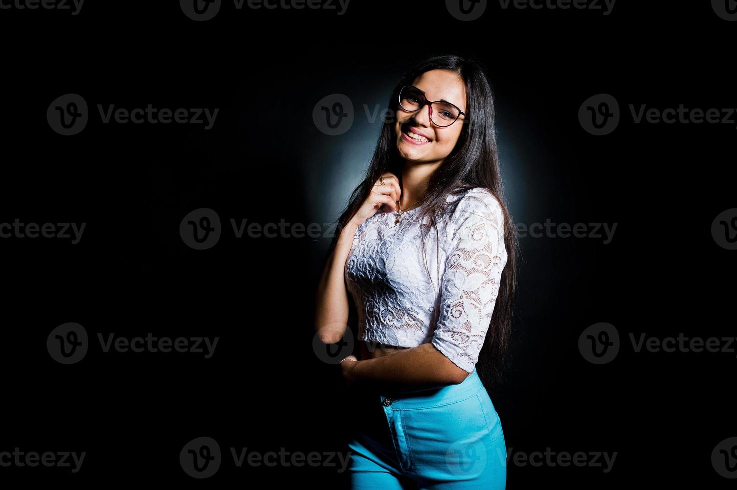 ritratto di una giovane donna attraente in top bianco e pantaloni blu in posa con i suoi occhiali al buio. foto