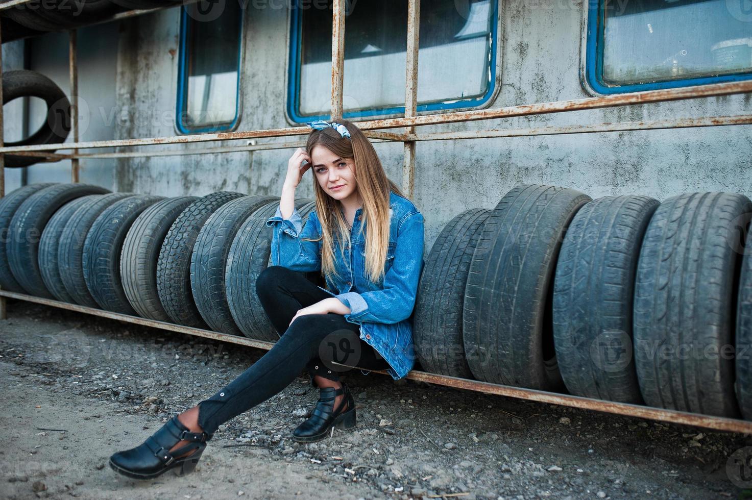 giovane ragazza hipster in giacca di jeans e sciarpa per la testa nella zona di montaggio dei pneumatici. foto