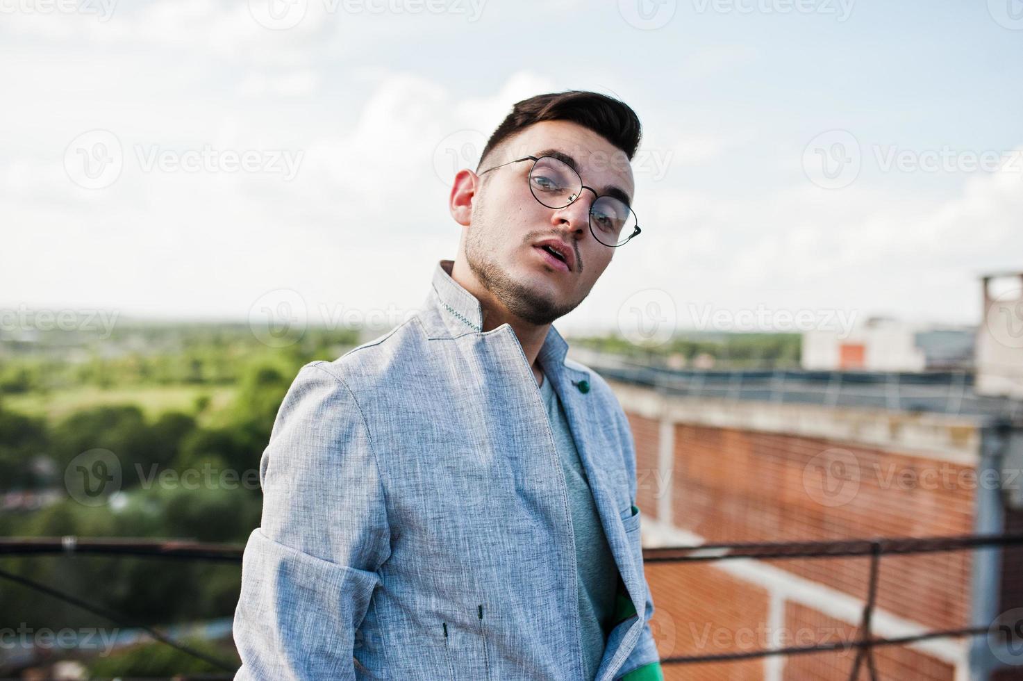 sognatore elegante uomo macho in abito grigio e occhiali posato sul tetto. foto