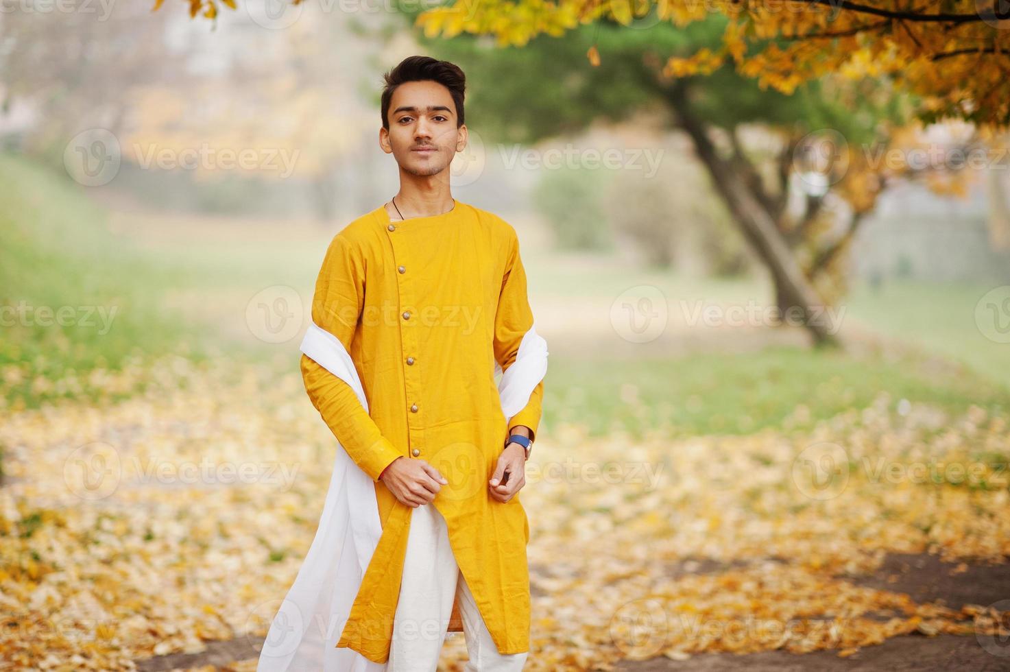 uomo indiano alla moda in abiti tradizionali gialli con sciarpa bianca poste all'aperto contro l'albero delle foglie di autunno. foto