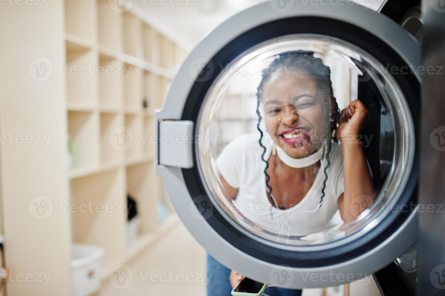 divertente ritratto di allegra donna afroamericana vicino alla lavatrice nella lavanderia self-service. foto