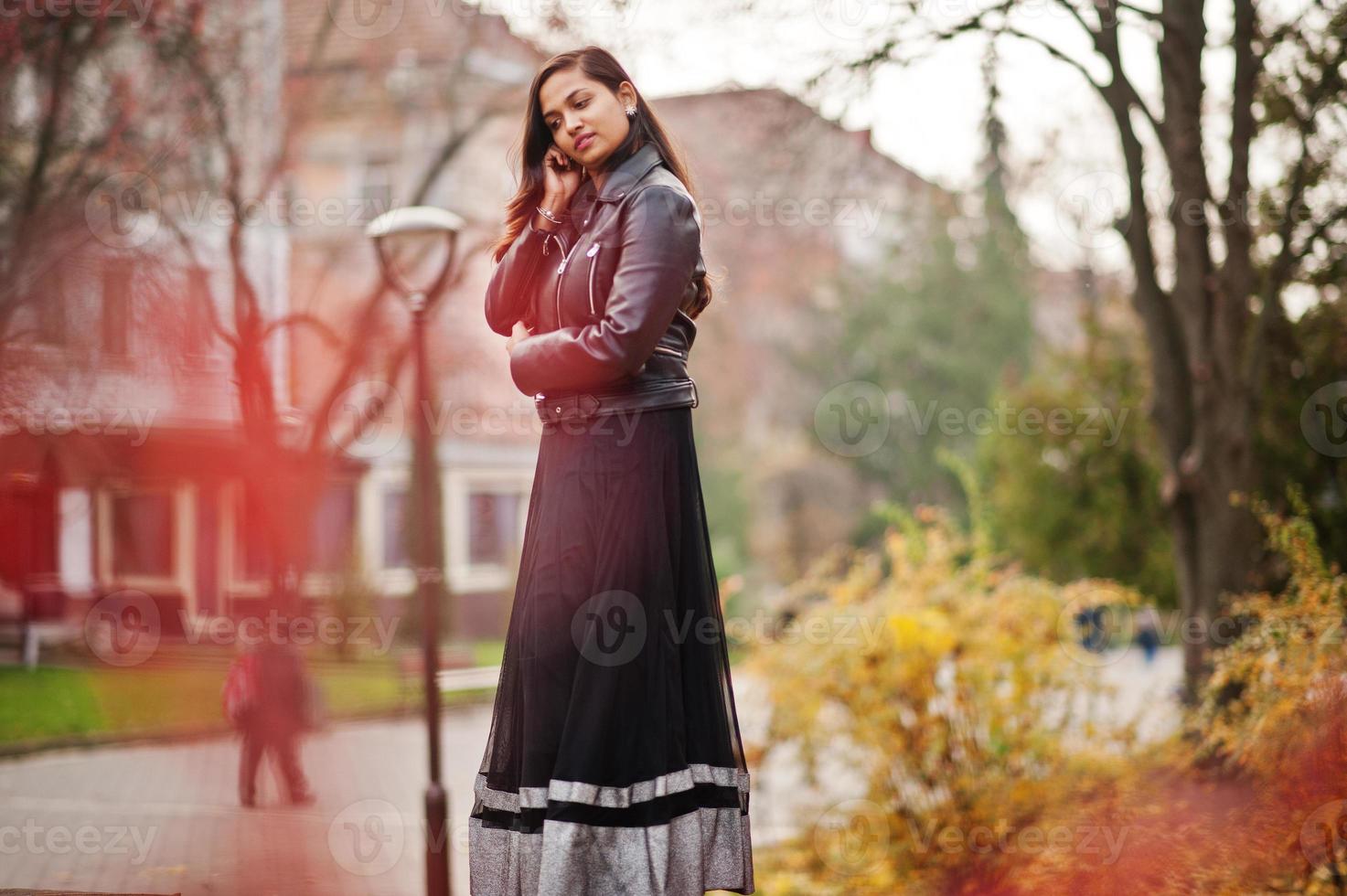 bella ragazza indiana in abito saree nero e giacca di pelle posata all'aperto in autunno street. foto