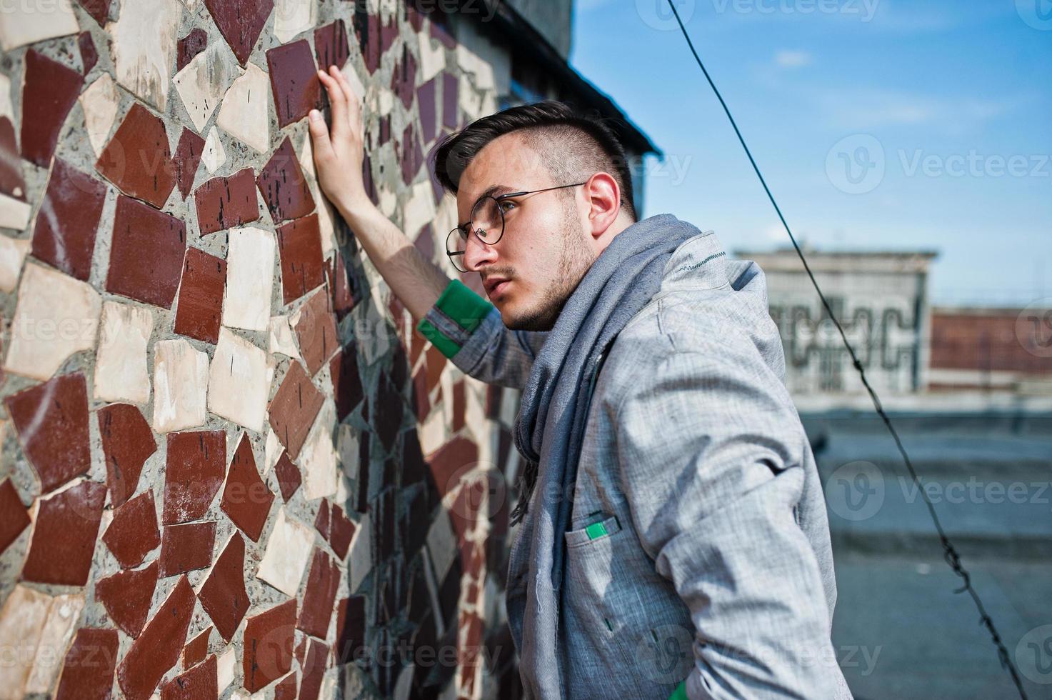 sognatore elegante uomo macho in abito grigio, sciarpa e occhiali posati sul tetto. foto