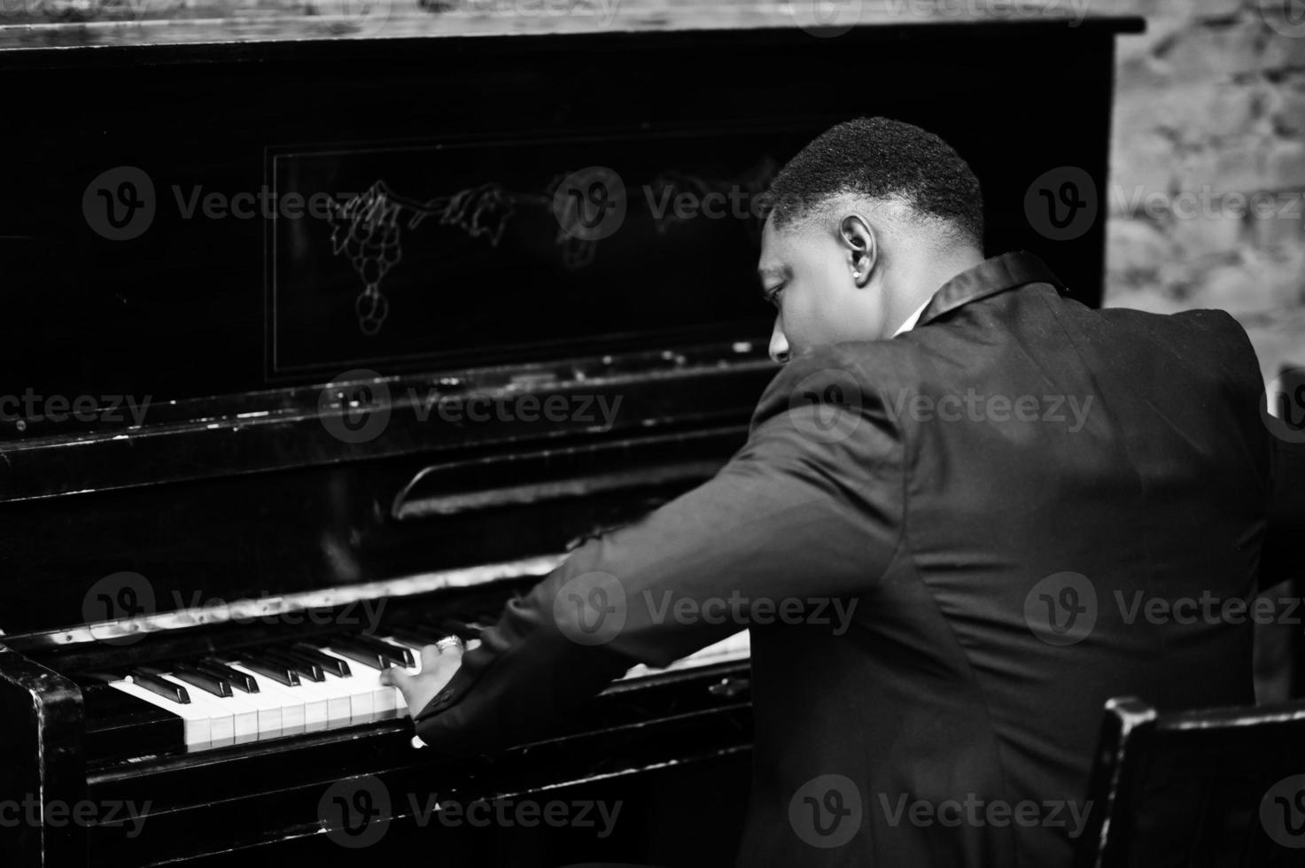 parte posteriore di un uomo afroamericano forte e potente in abito nero suona il pianoforte. foto